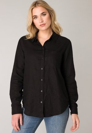 Zwarte langarm knopenhemd van textuurstof, met een kraag, borstzak en ronde zoom, gecombineerd met lichtblauwe jeans.
