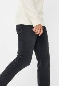 Jeans neri con una vestibilità slim, caratterizzati da una texture liscia e un classico design a cinque tasche, abbinati a un maglione chiaro in crema con texture.
