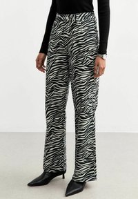 Zebra mönstrade vida byxor i svart och vitt denim med hög midja och knappstängning fram. Matchat med svarta spetsiga klackskor.