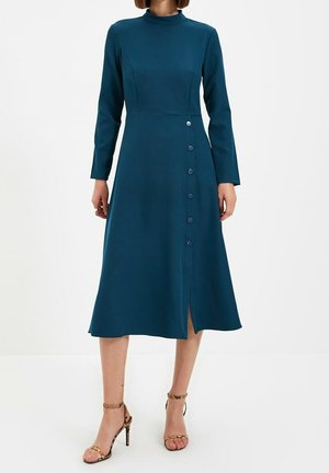 Długa sukienka z długim rękawem w kolorze zielononiebieskim, z wysokim dekoltem, dopasowaną górą, spódnicą w kształcie litery A oraz detalami z przodu zapinanymi na guziki; gładka faktura, długość do kolan.