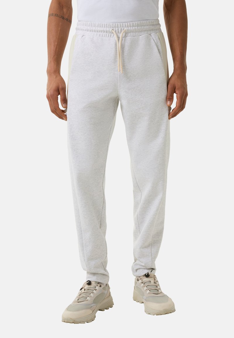 Helle graue Baumwoll-Jogginghosen mit elastischem Bund, Kordelzug und Seitentaschen, kombiniert mit hellen Sportschuhen.