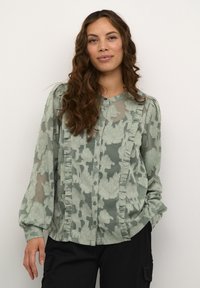 Blusa trasparente verde con motivo floreale, rifinita con volant lungo il davanti e le maniche, completata con un design con bottoni e scollo rotondo.