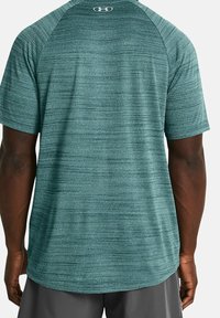 Miestenské športové tričko z textúrovanej tkaniny v odtieni teal. Má krátke rukávy, zaoblený lem a malé logo na hornej časti chrbta.