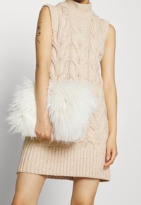 Abito senza maniche lavorato a maglia di un tenue rosa con motivi a treccia, abbinato a una borsa a tracolla in pelliccia sintetica bianca e soffice. Tessuto testurizzato con orlo a coste.