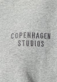 Grauer Pullover aus weichem Material. Mit einem gestickten Logo "COPENHAGEN STUDIOS" in dunklen Fäden. Einfaches, rundes Design des Halsausschnitts.