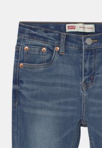 Levi's skinny taper jeans i medelblå denim. Har koppardetaljer, fem fickor och kontrasterande sömmar. Slät textur, smal design.