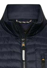 Marineblaue gesteppte Jacke mit Kragen, schwarzem Reißverschluss und kleinem reflektierendem Streifen am Reißverschlusszipper.