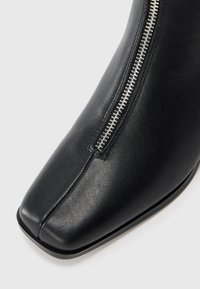 Black leather boot with square toe and silver zipper detail on the front upper side.