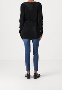 Musta ribbattu pitkähihainen toppi, jossa on istuva vyötärö ja avara pääntie, yhdistettynä sinisiin istuviin farkkuihin ja mustiin korkea-kantaiseen kenkään.