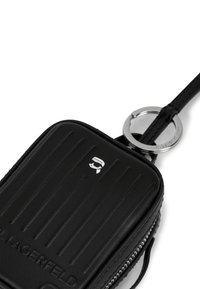 Schwarzes rechteckiges Lederetui mit gerippter Textur, silbernem Reißverschluss, Schlüsselring und Logo mit einem stilisierten Gesicht auf der Vorderseite.
