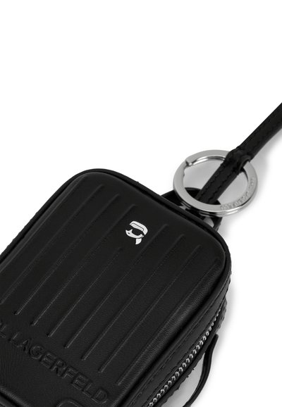 Pochette rectangulaire en cuir noir avec texture à rainures, fermeture éclair argentée, porte-clés et logo présentant un visage stylisé à l'avant.