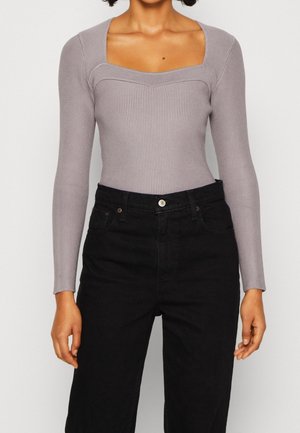 Langärmliger, gerippter Bodysuit in Hellgrau mit quadratischem Ausschnitt und taillierter Passform, kombiniert mit hochgeschnittenen schwarzen Jeans.