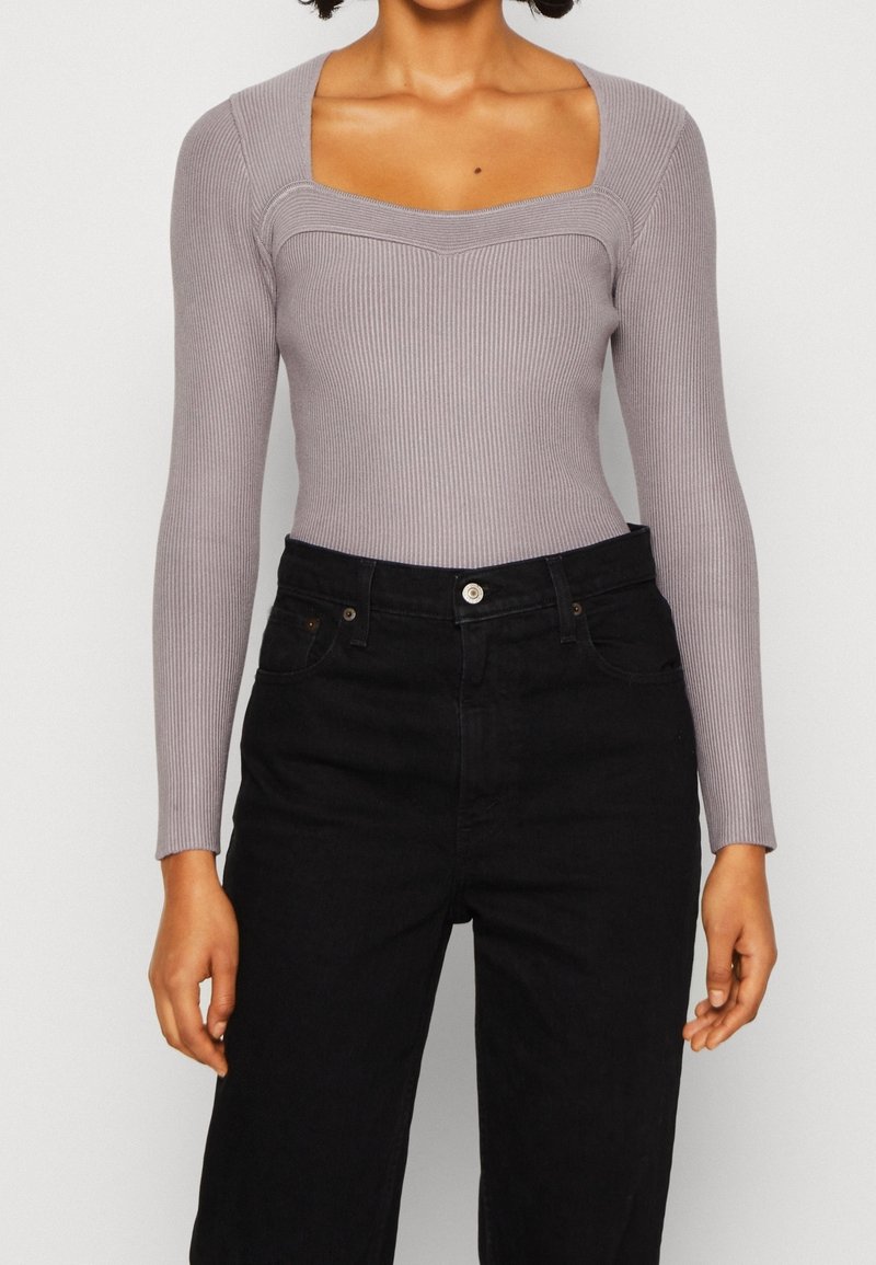 Langärmliger, gerippter Bodysuit in Hellgrau mit quadratischem Ausschnitt und taillierter Passform, kombiniert mit hochgeschnittenen schwarzen Jeans.