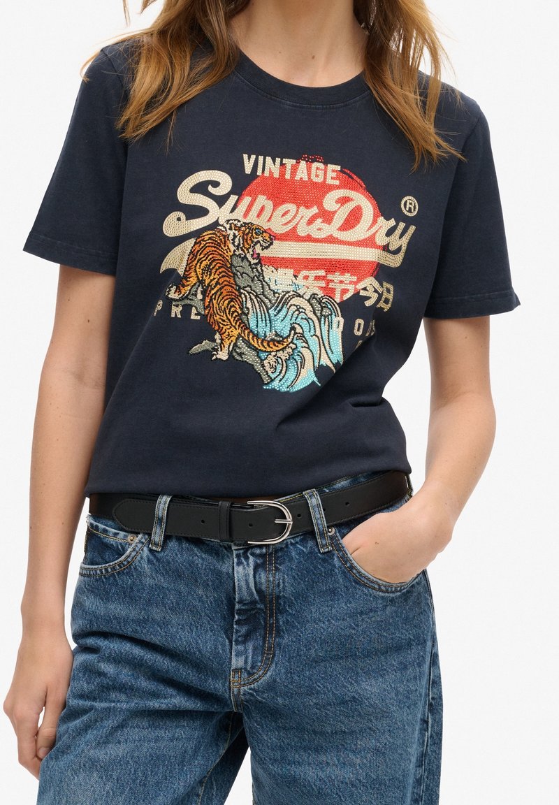 Mörkblå bomullströja med en grafisk design som har en tiger och vågor. Korta ärmar och rund halsringning, matchad med högmidjade jeans.