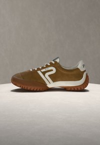 Baskets en daim marron avec des détails blancs, un design à lacets et une semelle marron texturée sur une surface et un fond neutres.