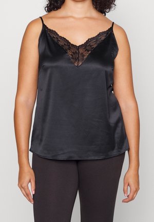 Kvinde iført sort satin camisole med blondekant ved V-hals og tynde skulderstropper, kombineret med sorte bukser.