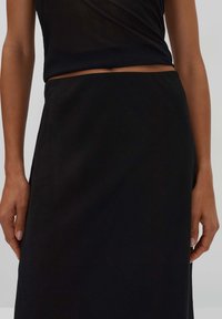 Schwarze, knielange Rock mit glatter, weicher Textur und elastischem Bund; kombiniert mit einem taillierten, schwarzen ärmellosen Oberteil.