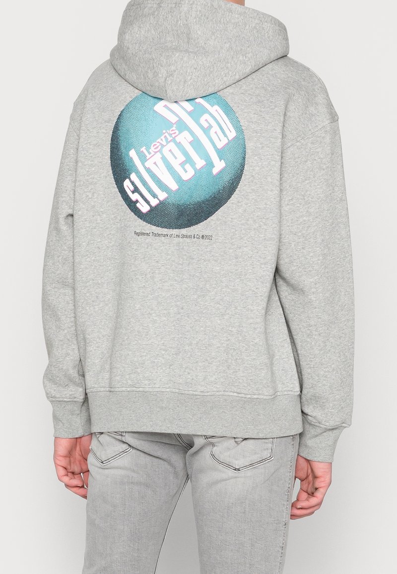 Sudadera con capucha gris con un estampado gráfico circular en verde azulado y rosa, con el texto "Levi's Silver Lab", sobre una tela suave y texturizada.