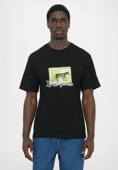 Μαύρο βαμβακερό μπλουζάκι με γραφικό κίτρινου χρώματος σε στιλ σφραγίδας, που έχει ένα μαύρο σχέδιο ζώου και το κείμενο "Les Benjamins" από κάτω.
