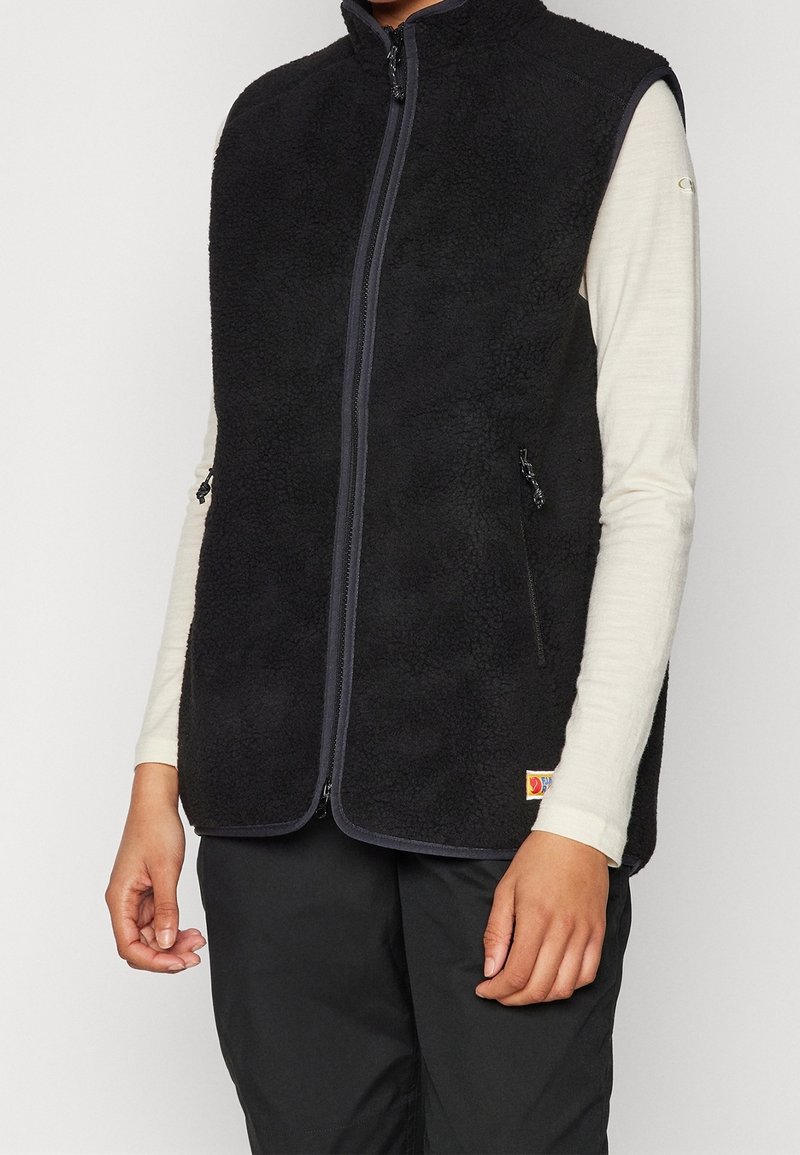 Schwarze Fleece-Weste mit hohem Kragen, durchgehendem Reißverschluss, Seitentaschen und kontrastierenden Einsätzen. Strukturierter Stoff mit weichem Griff und ohne Ärmel.