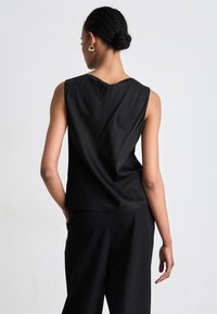 Melnā bezpalmu krekla augšdaļa, izgatavota no gludas auduma, ar brīvu piegriezumu un apaļu kakla izgriezumu, ar izkārtotu aizmugures dizainu.