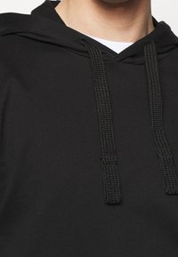 Svart huvtröja i texturerad tyg med dragsko i kragen. Har tjocka, flätade snören och en klassisk känguruficka.