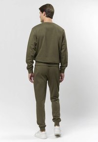 Olivengrønn genser og matchende joggebukser i et mykt stoff. Genseren har rund hals og ribbede mansjetter; buksene har elastiske mansjetter og sitter tett.