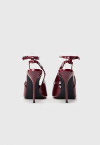 Burgundijas patenta ādas augstpapēžu sandales ar potīšu siksniņām, atvērtu purngalu un šauriem stiletto papēžiem. Gluda tekstūra ar spīdīgu apdari.