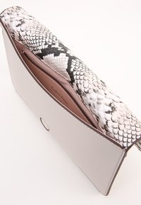 Clutch de sobre de cuero blanco con una solapa de estampado de serpiente en blanco y negro texturizado. El interior cuenta con un forro marrón y el logo "Calvin Klein".