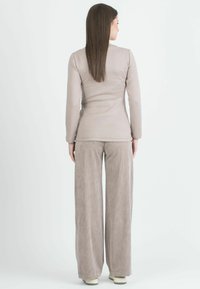 Maglietta a maniche lunghe color beige chiaro abbinata a pantaloni in corduroy ampi e strutturati dello stesso colore, caratterizzati da gambe larghe e sottili righe verticali.