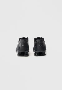 Sapatilhas desportivas pretas com um upper texturizado, almofadado distinto no calcanhar e um design elegante. As solas apresentam estruturas em espiral visíveis.