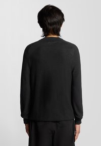 Maglione nero a maniche lunghe con tessuto testurizzato, dotato di spalle a raglan e polsini a coste. Dettaglio del logo sottile sulla parte superiore della schiena.