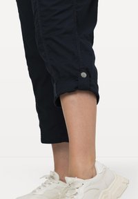 Marina korta byxor med uppvikta ärmar och detalj i silverknappar, tillverkade av ett lätt material, i kombination med vita sneakers.
