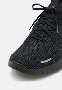 Černá sportovní bota s texturovaným textilním svrškem, plochými černými tkaničkami a polstrovanou černou gumovou podrážkou se decentním reflexním akcentem.