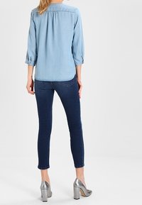 Helles blauen Jeanshemd mit drei Viertelärmeln, kombiniert mit dunkelblauen Skinny Jeans und silbernen High Heels.