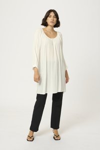 Witte lange mouw tuniek met ronde hals en gathered detail. Gecombineerd met zwarte rechte broek en platte zwarte sandalen.
