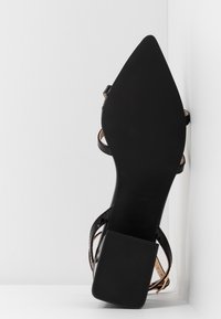 Sandale à talon haut en cuir verni noir avec un bout pointu, des fines lanières et une semelle en caoutchouc noir texturé pour une meilleure adhérence.