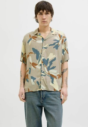 Chemise à manches courtes, à boutons, en beige avec des motifs floraux abstraits en bleu, marron et crème. Légère, coupe décontractée, texture douce.