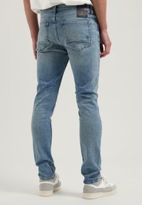 Vaqueros de mezclilla de ajuste slim fit en azul claro, con una cintura de altura media, diseño de cinco bolsillos y un ligero agotamiento. Etiqueta visible en la parte trasera de la cintura.