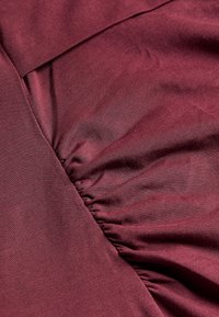 Bordeaux stof met een gladde textuur; heeft verzamelde details en een vlak gedeelte, met een lichte glans en rek.
