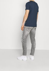Mörkblå t-shirt med kort ärm, tillsammans med ljusgrå slim-fit jeans med en sliten yta och vita sneakers.