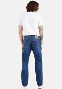 Jeans de mezclilla azul con corte recto, que presentan una etiqueta de cuero marrón en la parte trasera y dos bolsillos traseros, llevados con una camiseta blanca.