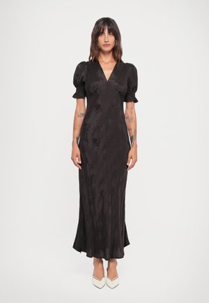 Vestido negro midi con mangas cortas abullonadas, escote en V profundo, tejido texturizado y silueta fluida, combinado con tacones blancos de punta afilada.