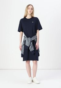 Navy blue t-shirt dress with short sleeves and a relaxed fit, paired with a patterned grey sweater tied around the waist. White sneakers.