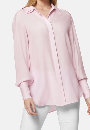 Blouse rose clair à manches longues avec un col pointu, fermeture à boutons sur le devant et tissu lisse. Présente un ourlet légèrement courbé et une coupe décontractée.