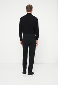 Črna prilegajoča se turtleneck majica v kombinaciji s črnimi taperjšimi hlačami, ki imajo zadnji žep. Obuta s črnimi in belimi supergami. Teksturovana tkanina.
