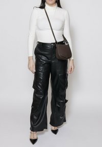 Pantaloni cargo in pelle nera con tasche laterali, abbinati a un dolcevita bianco aderente e a una borsa a spalla marrone. Tacchi a punta neri completano l'outfit.