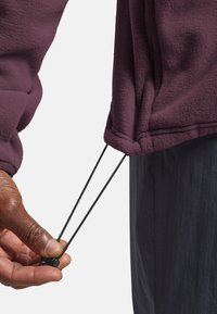 Fleecejacke in Dunkellila mit elastischem Zugband am Saum. Mit Handgriffen und schwarzem Kordelzug zur Anpassung. Die Oberfläche ist strukturiert.