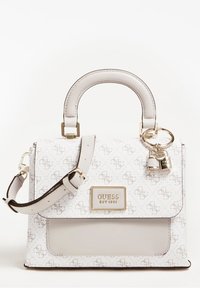 Witte Guess-handtas met beige logopatroon, bovenhandvat, verstelbare schouderband, gouden hardware en decoratieve sleutelhanger in de vorm van een hangslot.