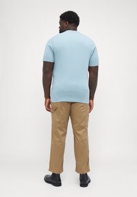 Lyseblå kortermet polo skjorte kombinert med beige cargo bukser og svarte ankelboots; glatt stoff, tettsittende design og bruks lommer.